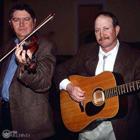 Two Musicians pose with a guitar and fiddle.