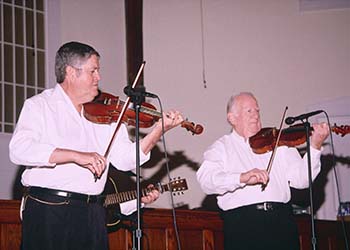 Two fiddle players and a guitarist on stage performing