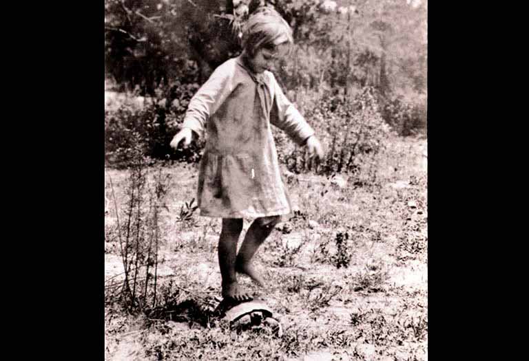 A little girl stands on the back of a gopher turtle.