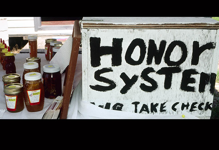 A table laid out with jars of honey and a sign that reads: Honor System, take check.