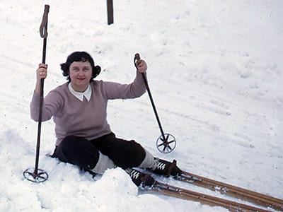 Leona sitting in the snow with skis. (1950s).